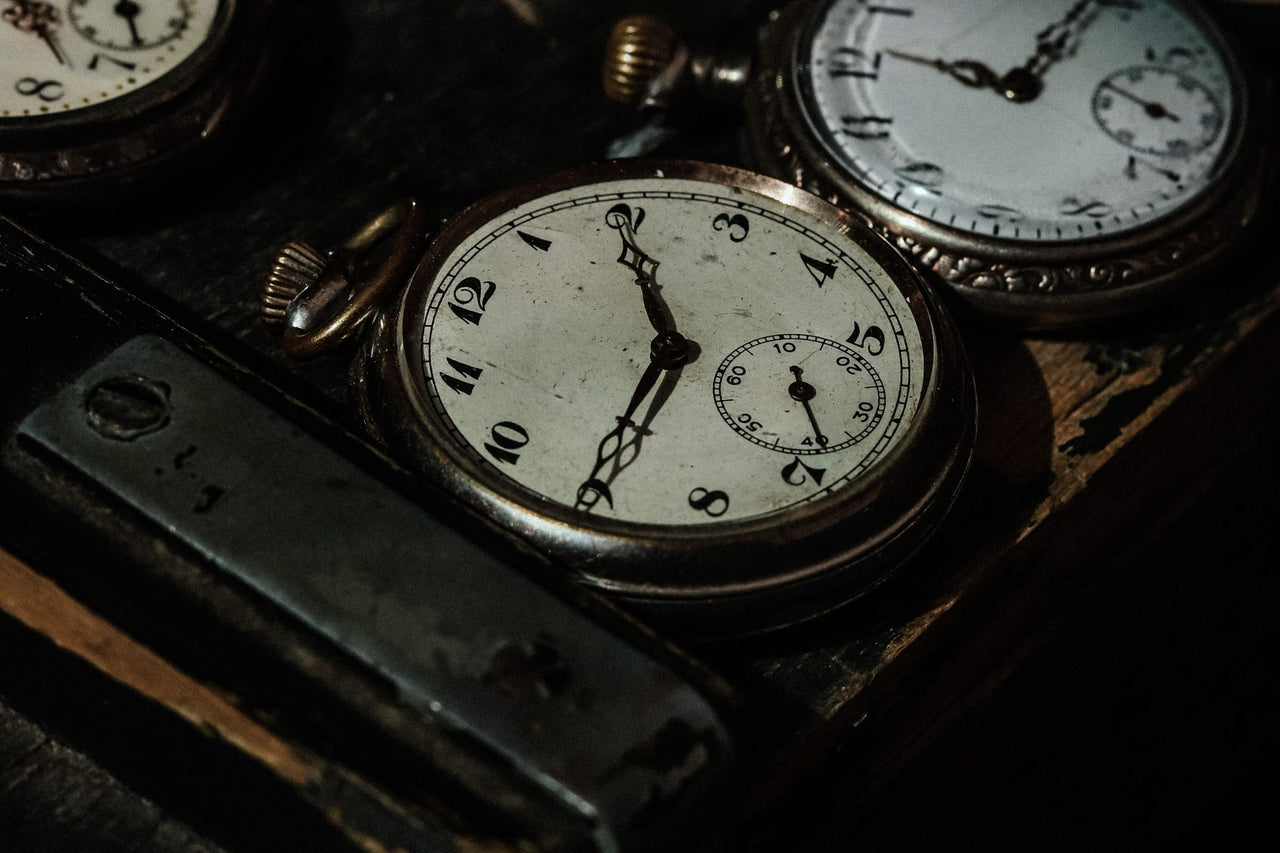 Antique pocket watches with aged dials resting on a dark wooden
workbench
